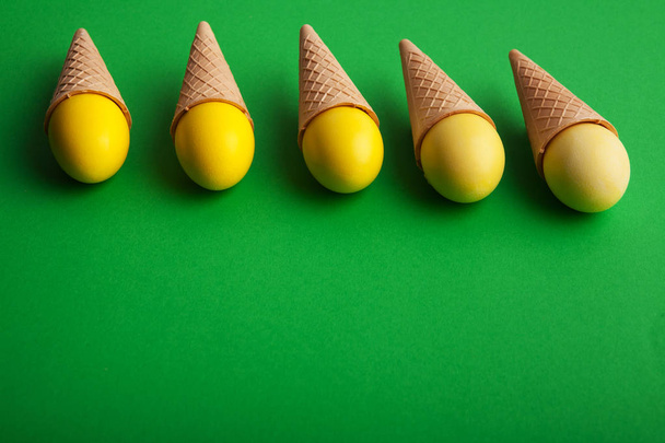 Yellow easter eggs in waffle cones on green background - Foto, Imagen