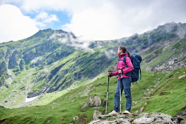 Backpacker kobieta odpoczynku podczas wędrówki w stojący na szczycie skały cieszyć się wspaniały widok na góry krajobraz wokół lato relaks odpoczynek camping wycieczkowicz hobby styl życia przyjemność przyrody. - Zdjęcie, obraz