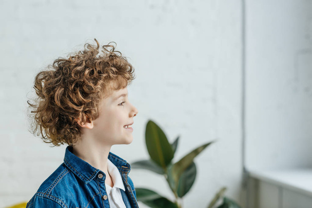 Smiling little boy with curly hair looking in window - Фото, зображення