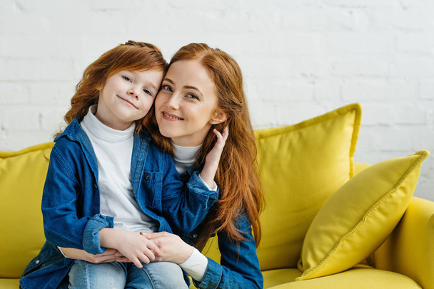 Redhead woman embracing her daughter on sofa - Photo, Image