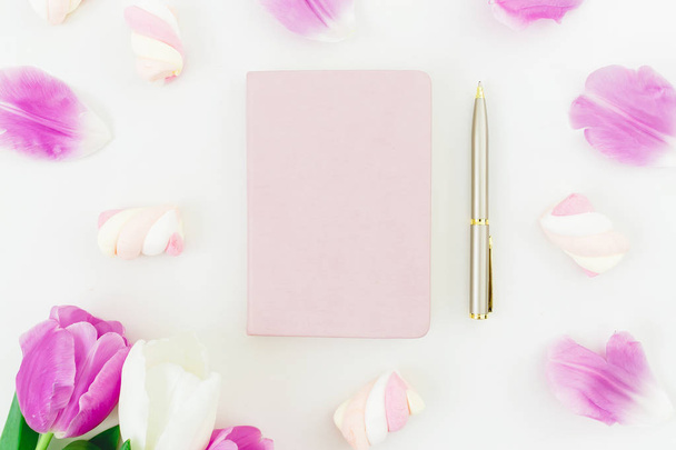 Top view of pink notebook and golden pen surrounded by vibrant tulips and marshmallows  - Valokuva, kuva