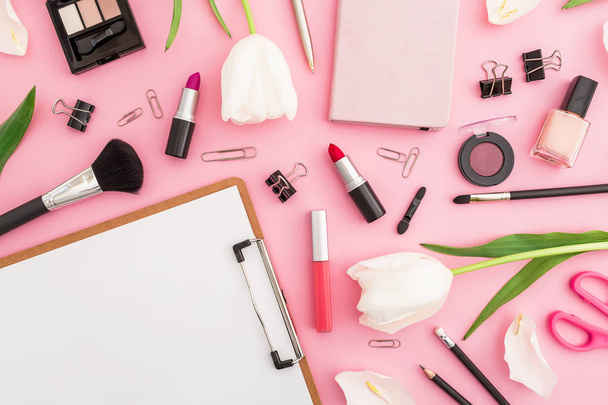 Bovenaanzicht van puinhoop op roze tafel met cosmetica, briefpapier en tulpen - Foto, afbeelding