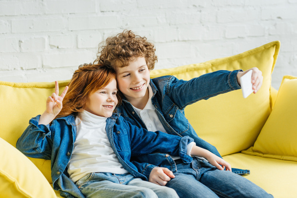 Smiling children taking selfie while sitting on sofa - Foto, immagini