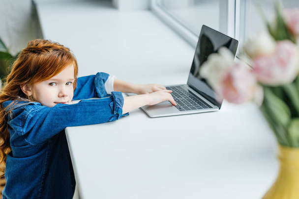 Piccolo bambino rossa utilizzando computer portatile sul davanzale della finestra
 - Foto, immagini