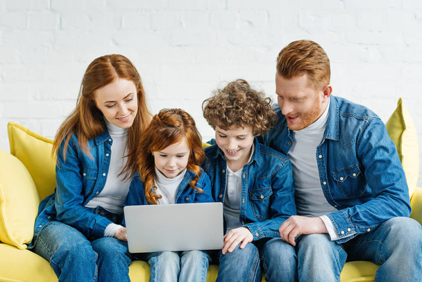 Redhead family sitting on sofa and looking at laptop screen - Фото, зображення