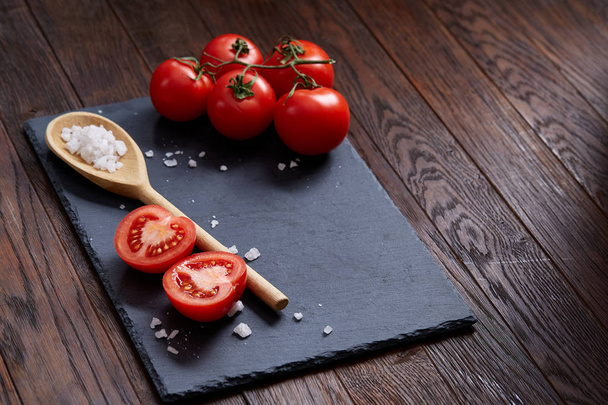 Vegetarian still life with fresh grape tomatoes, pepper and salt in wooden spoon on wooden background, selective focus - Fotó, kép