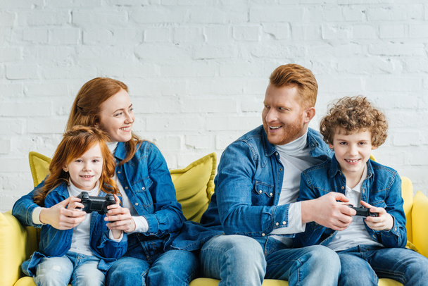Kids and parents playing video game while sitting on sofa - Fotó, kép