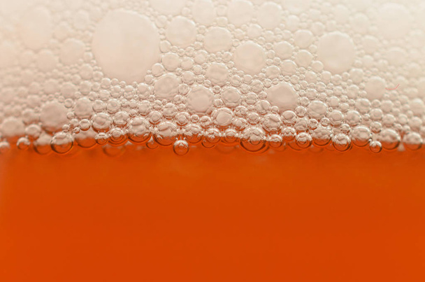 Φυσαλίδες από ένα κοντινό πλάνο αφρό μπύρα σε μισό ποτήρι. - Φωτογραφία, εικόνα
