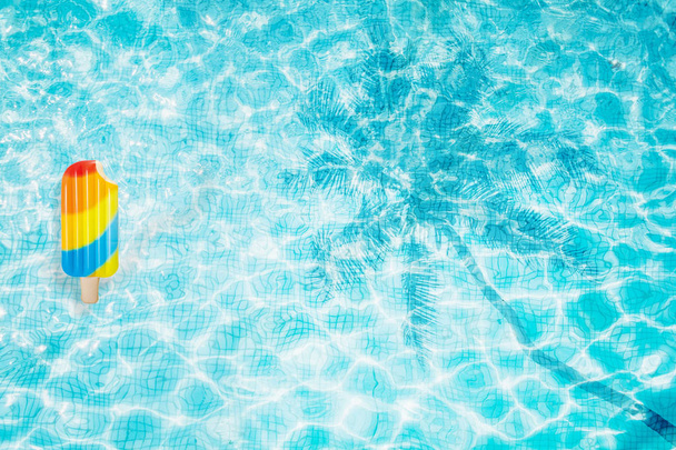 Vista superior del fondo de la piscina con helado inflable de colores y sombra de palma
 - Foto, imagen