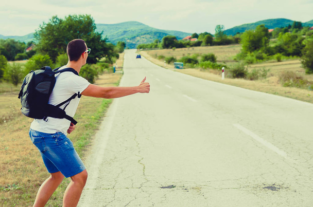 Hitchhiking traveler try to stop car on the mountain road - Photo, Image