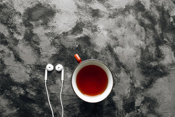 белые современные наушники и чашка чая на фоне черного камня
 - Фото, изображение