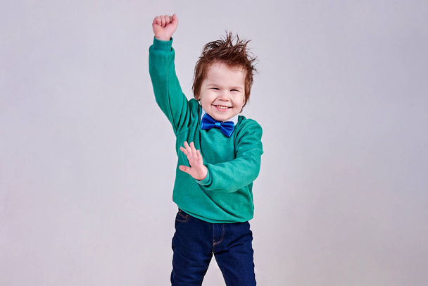 Przystojny, mały chłopiec, noszenie muchą niebieski i zielony sweter, tańce i uśmiecha się - Zdjęcie, obraz