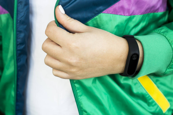Female hand with a fitness bracelet. In a sports bright green jacket for sports. Healthy lifestyle and fitness concept - Foto, Bild
