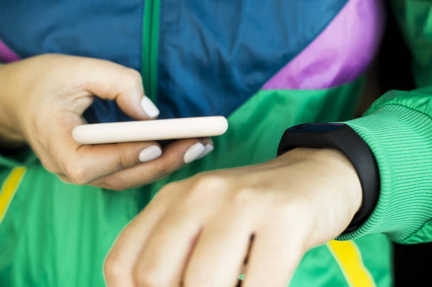 Жінка натискає на свій смартфон, щоб відрегулювати фітнес-браслет. У спортивній яскраво-зеленій куртці для спорту. Здоровий спосіб життя та концепція фітнесу
 - Фото, зображення