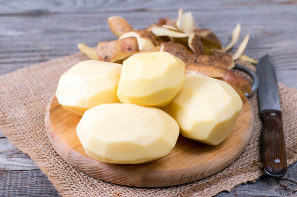 Чистый картофель с кожурой и ножом на деревянном столе
 - Фото, изображение