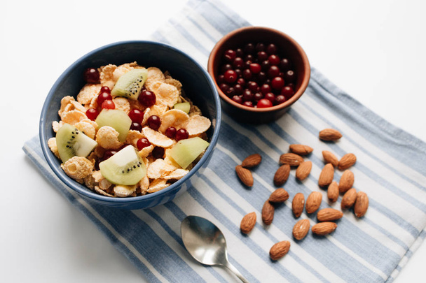 delicious crispy cornflakes with kiwi pieces and cranberries in bowl, almonds on dish cloth, closeup, healthy breakfast  - Valokuva, kuva