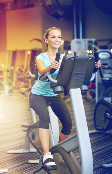 smiling woman exercising on exercise bike in gym - Foto, afbeelding