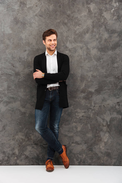 Cheerful young businessman standing over grey wall - Fotografie, Obrázek