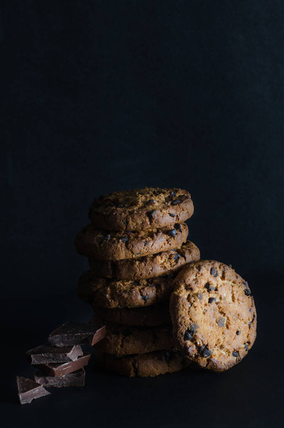 Chocolate chip cookies and chocolate pieces on dark background. - Fotó, kép