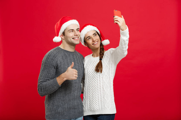 Christmas Concept - Young attractive couple taking a selfie by mobile phone celebrating in Christmas day - Zdjęcie, obraz