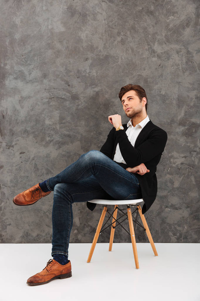 Thoughtful young businessman sitting over grey wall - Zdjęcie, obraz