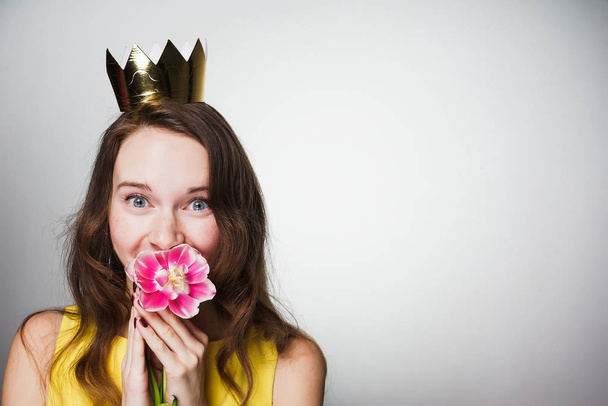 beautiful blue-eyed girl holding a pink flower, smiling, wearing a golden crown - Foto, afbeelding