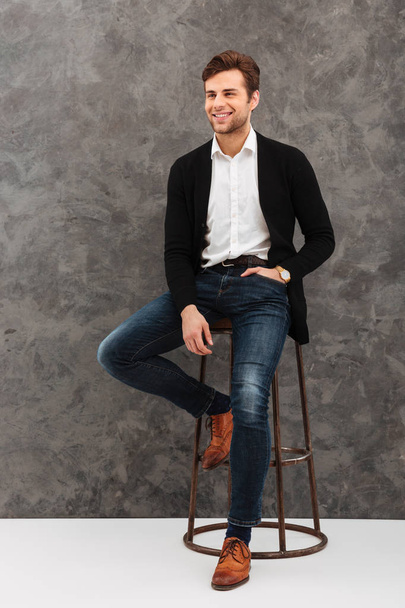 Cheerful young businessman sitting over grey wall - Foto, Imagem