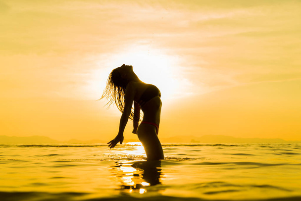 Silhouette of young girl in the water that splashing their hair  - Фото, изображение