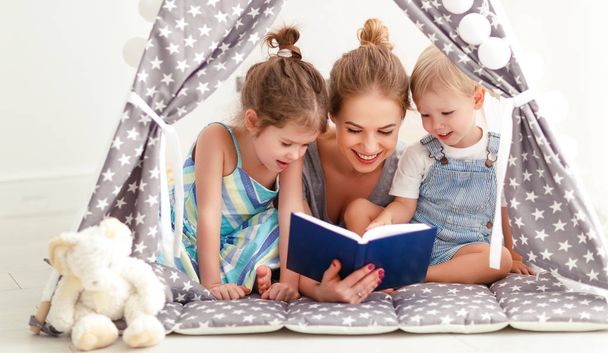 familia madre leyendo a los niños libro en tienda de campaña en hom
 - Foto, Imagen