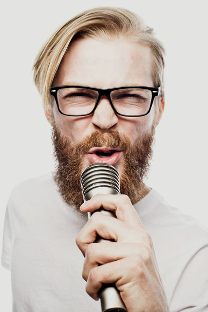 bearded man singing to the microphone. Emotional portrait of an attractive guy with a beard on a white background - Foto, afbeelding