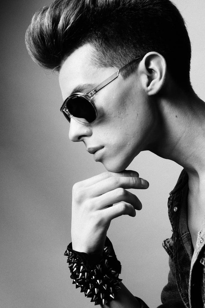 Handsome young man model with fashion haircut and sunglasses posing in studio. Black and white picture. - Fotoğraf, Görsel