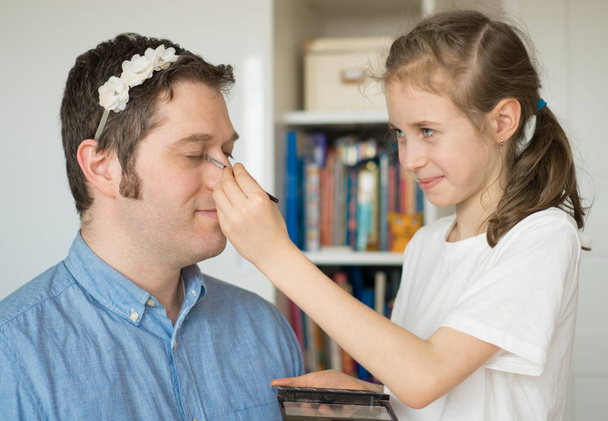 Linda niña haciendo maquillaje a su padre. - Foto, Imagen