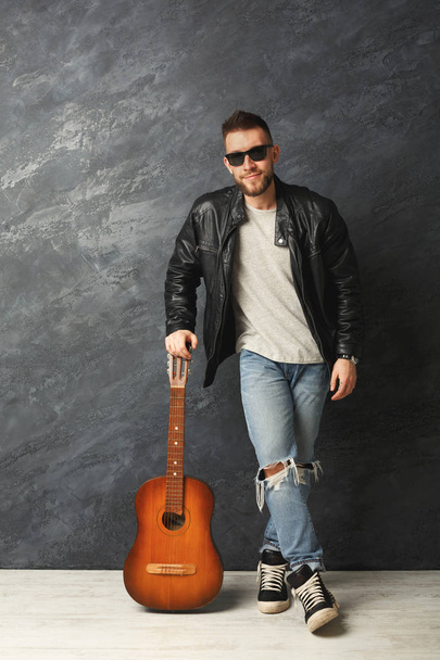 Handsome smiling man with guitar posing in studio - Fotó, kép