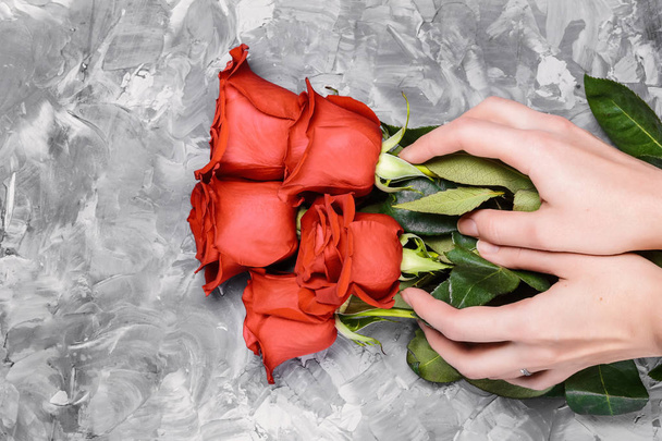 Five red roses in female hands on a gray concrete abstract background - Photo, Image