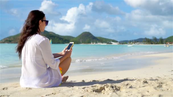 Mladá žena s chytrým telefonem během tropické dovolené na pláži. Krásná dívka na pláži s mobilem na karibském ostrově. SLOW MOTION - Záběry, video