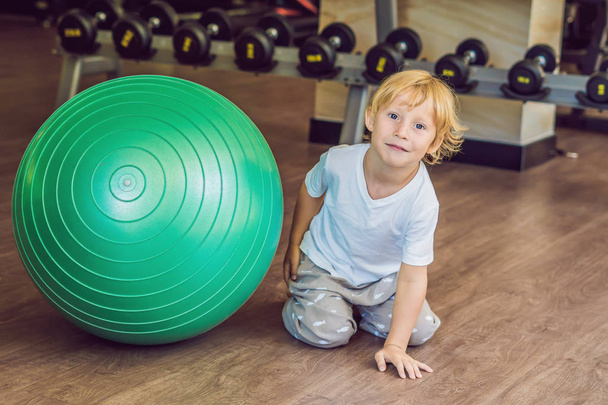 The boy is sitting near the fit ball in the gym. - Φωτογραφία, εικόνα
