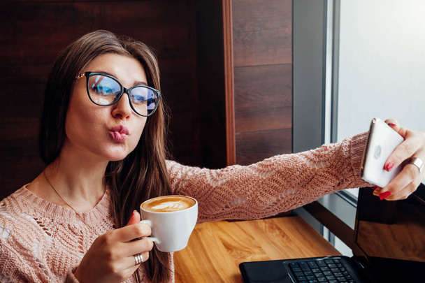 若いきれいな女性のフリーランサーは、selfie、カフェでコーヒーを楽しんでいます - 写真・画像
