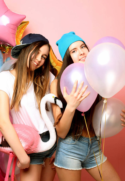 Two funny friends make grimace and have fun . Two emotional girls hold balloons and posing against pink wall. - Fotoğraf, Görsel