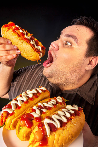 Hombre gordo comiendo perritos calientes de comida rápida. Desayuno para personas con sobrepeso
. - Foto, Imagen