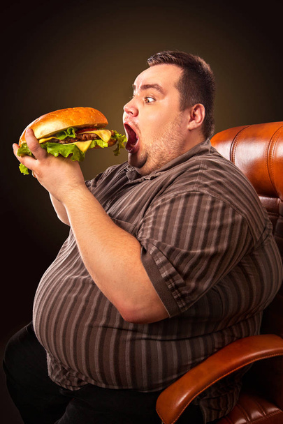 デブ男を食べるファーストフードのハンバーグ。太り過ぎの人の朝食. - 写真・画像
