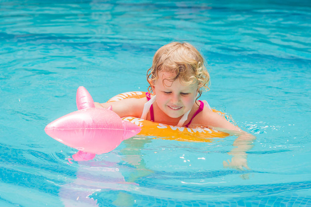 Прелестная маленькая девочка плавает в открытом бассейне и весело проводит время с замкнутым кругом. - Фото, изображение