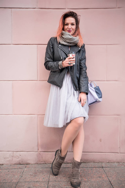 joven hermosa mujer posando de pie con taza de café en el fondo de la pared rosa en la calle de la ciudad
 - Foto, imagen