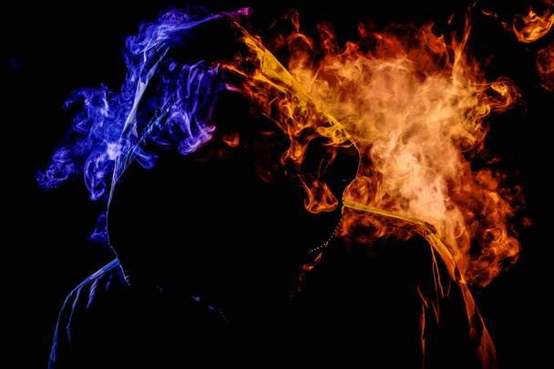 Młody człowiek w czarnym kapturem pali vape i wydech, kolor pomarańczowy i niebieski dym na czarnym tle na białym tle - Zdjęcie, obraz