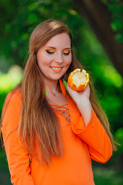 Portrait of pretty red hair woman holding juicy delicious orange at summer green park. - Foto, Imagen