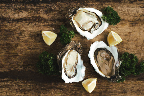 fresh just opened oysters and slice of lemon on rustic wooden background - Photo, Image