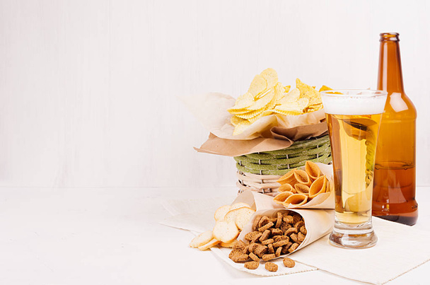 Wicker rustic basket with different junk food snacks and beer in wineglasses on white wood background. - Φωτογραφία, εικόνα