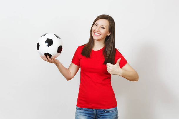 Европейская молодая веселая улыбающаяся женщина, футбольный фанат или игрок в красной форме, держащий футбольный мяч, показывающий большой палец, изолированный на белом фоне. Спорт, играть в футбол, болеть, здоровый образ жизни
. - Фото, изображение