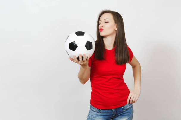 Mooie Europese jonge vrolijke gelukkige vrouw, voetbalfan of speler in het rode uniform greep kus klassieke voetbal geïsoleerd op een witte achtergrond. Sport spelen voetbal, gezondheid, gezonde levensstijl concept. - Foto, afbeelding