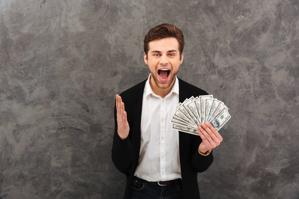 Excited happy young businessman holding money looking camera. - Фото, изображение