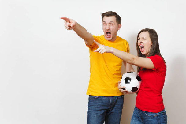 Sad upset young couple, woman, man, football fans in yellow red uniform with soccer ball cheer up team worries about losing team isolated on white background. Sport, family leisure, lifestyle concept. - 写真・画像
